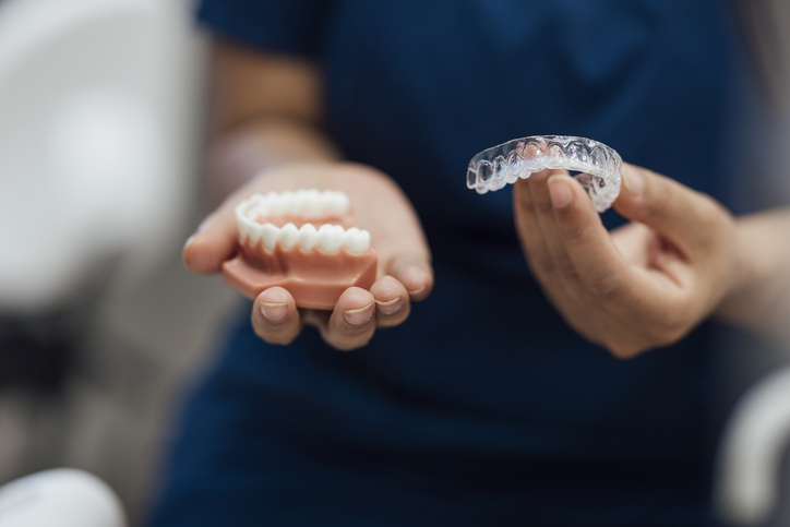 person holding a dental model of teeth and a clear aligner